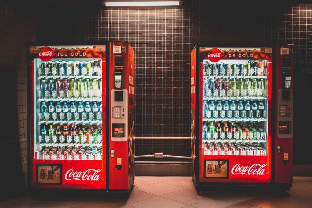 Two tall cold-drink vending machines in a tiled hall